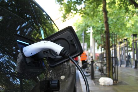 Ein Elektro-Auto das gerade geladen wird neben einer Straße mit Bäumen